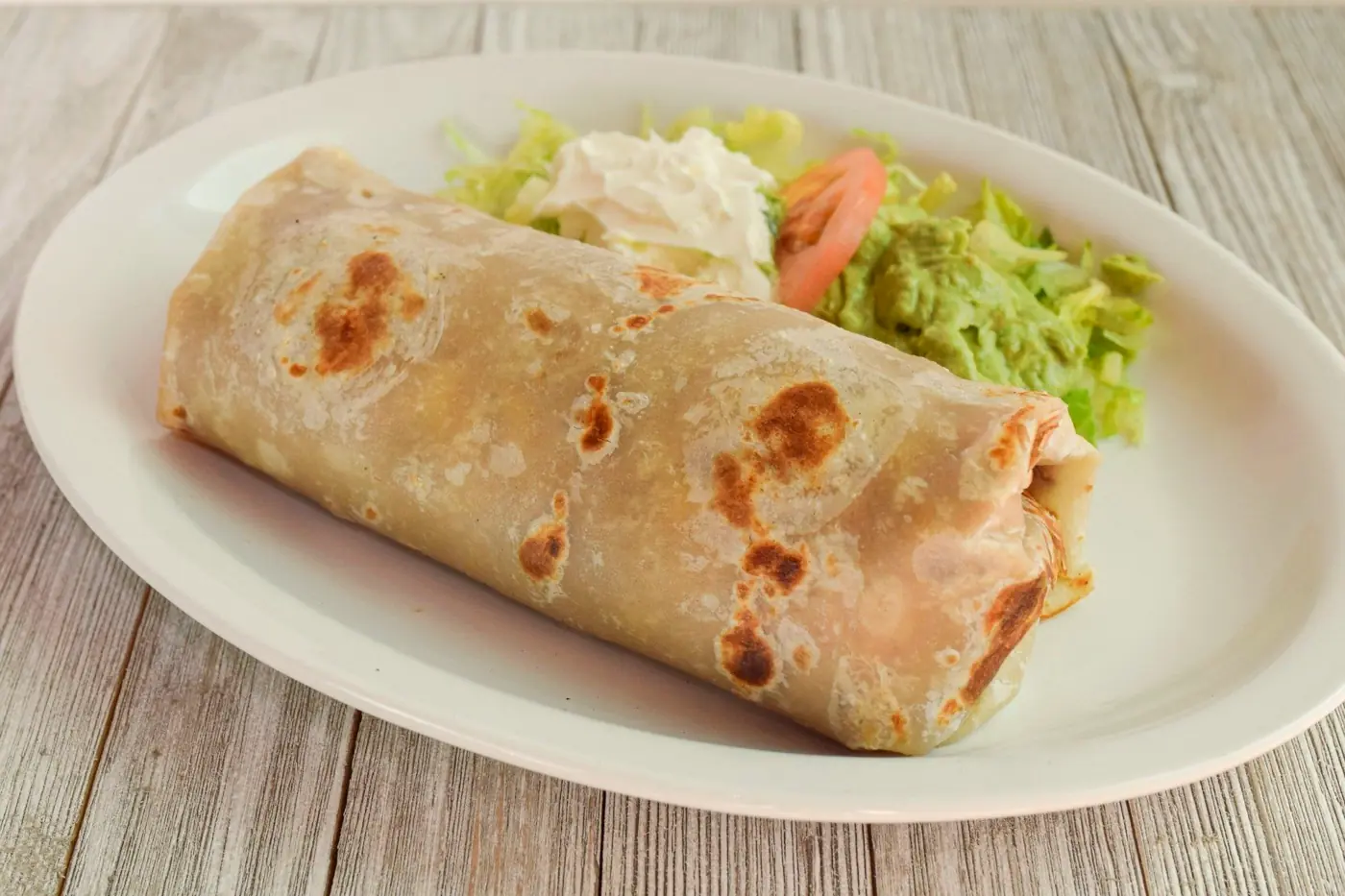 A large burrito with guacamole, sour cream and tomato on a white plate