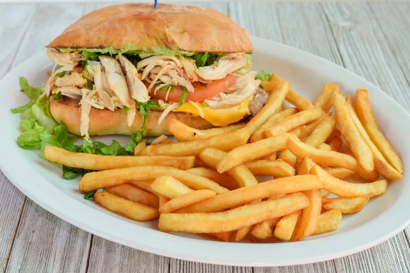 Shredded chicken torta with lettuce and tomato, piled beside a mound of fries
