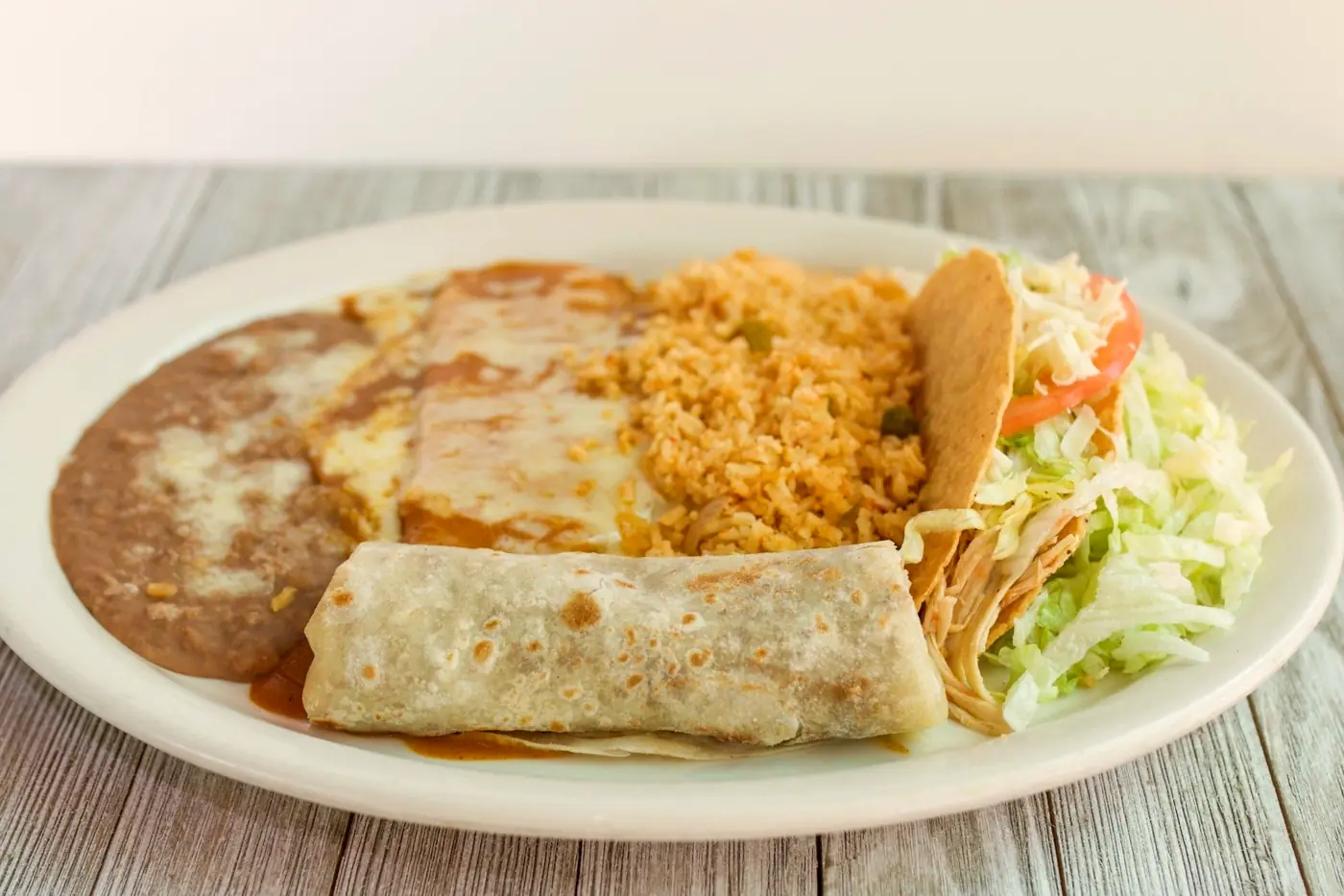 Combination plate with a burrito, a crispy taco, an enchilada, rice and refried beans