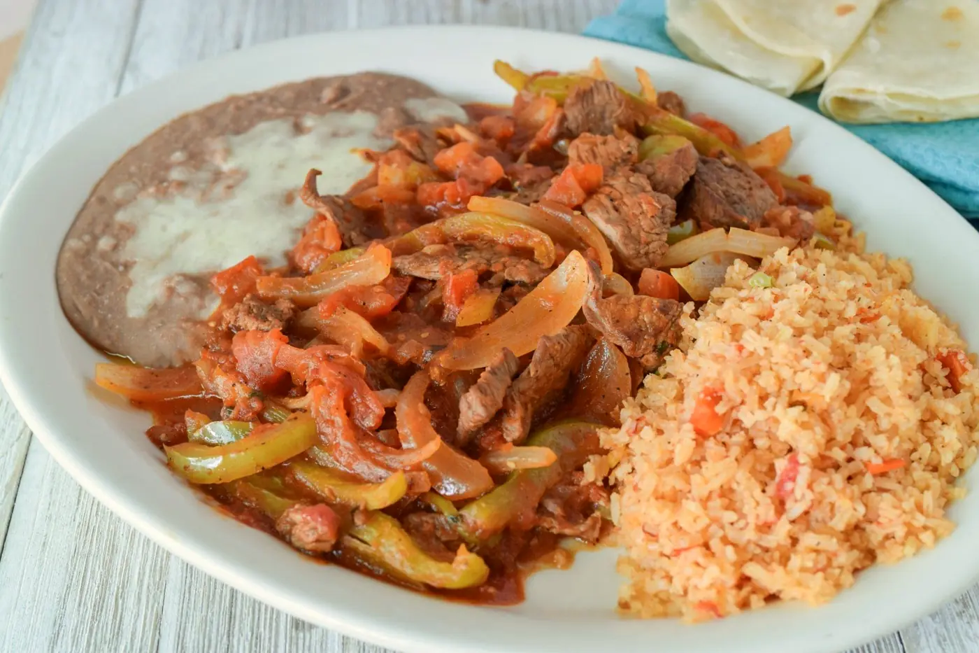 Strips of steak cooked with peppers, onions and tomato, served with rice and refried beans