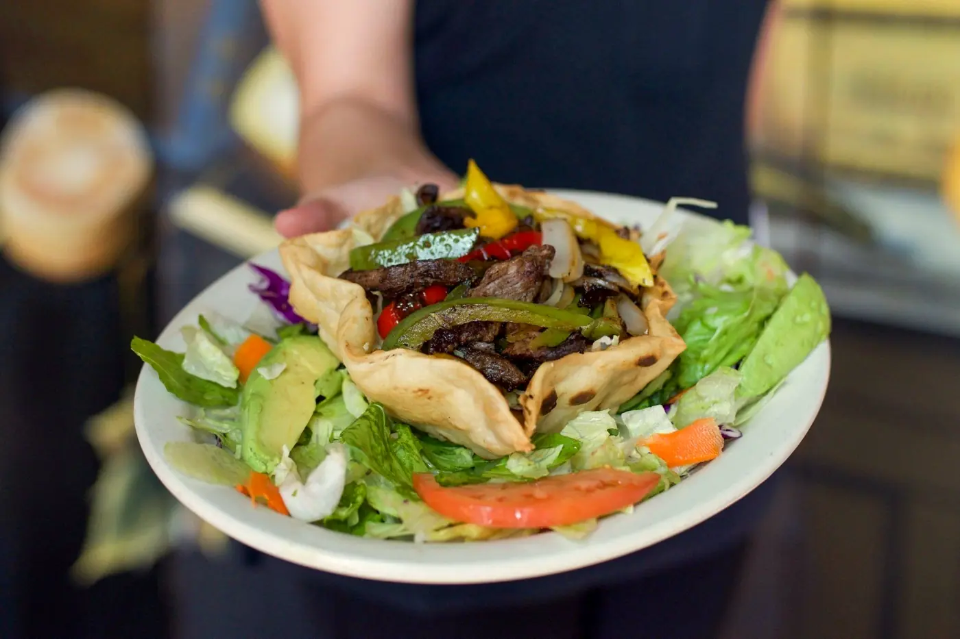 A taco salad in a crisp tortilla bowl, carried out by a server