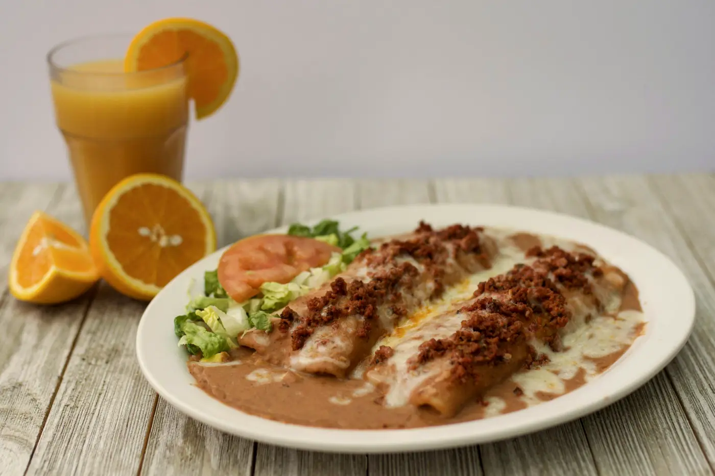 Two rolled enchiladas topped with sauce and meat, refried beans, salad and fresh orange juice